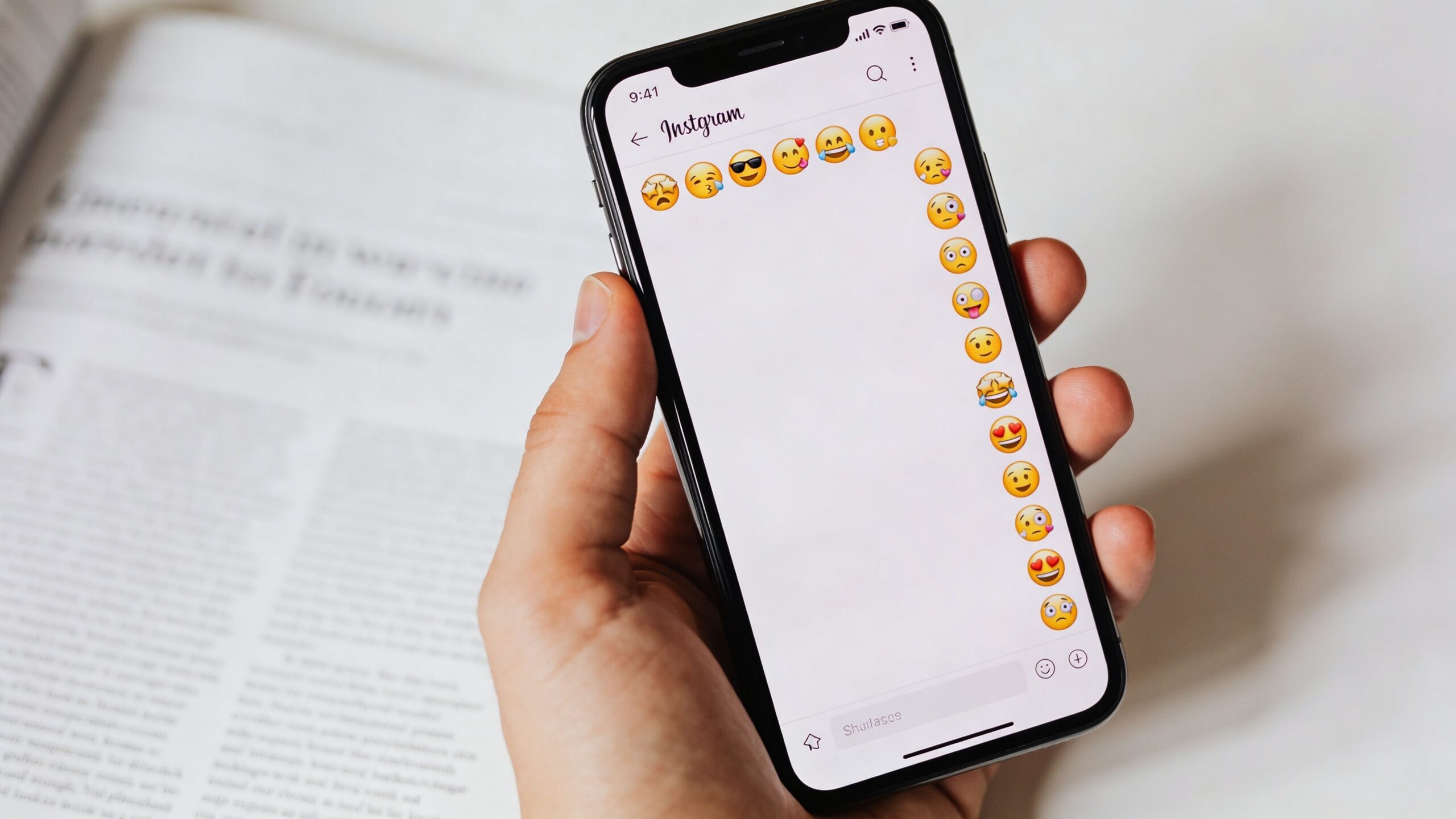 A person holding a smartphone displaying an Instagram chat screen filled with various expressive emoji faces.